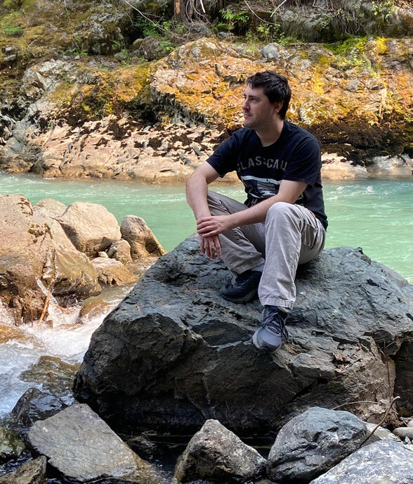 matthew sitting on a rock next to a river
